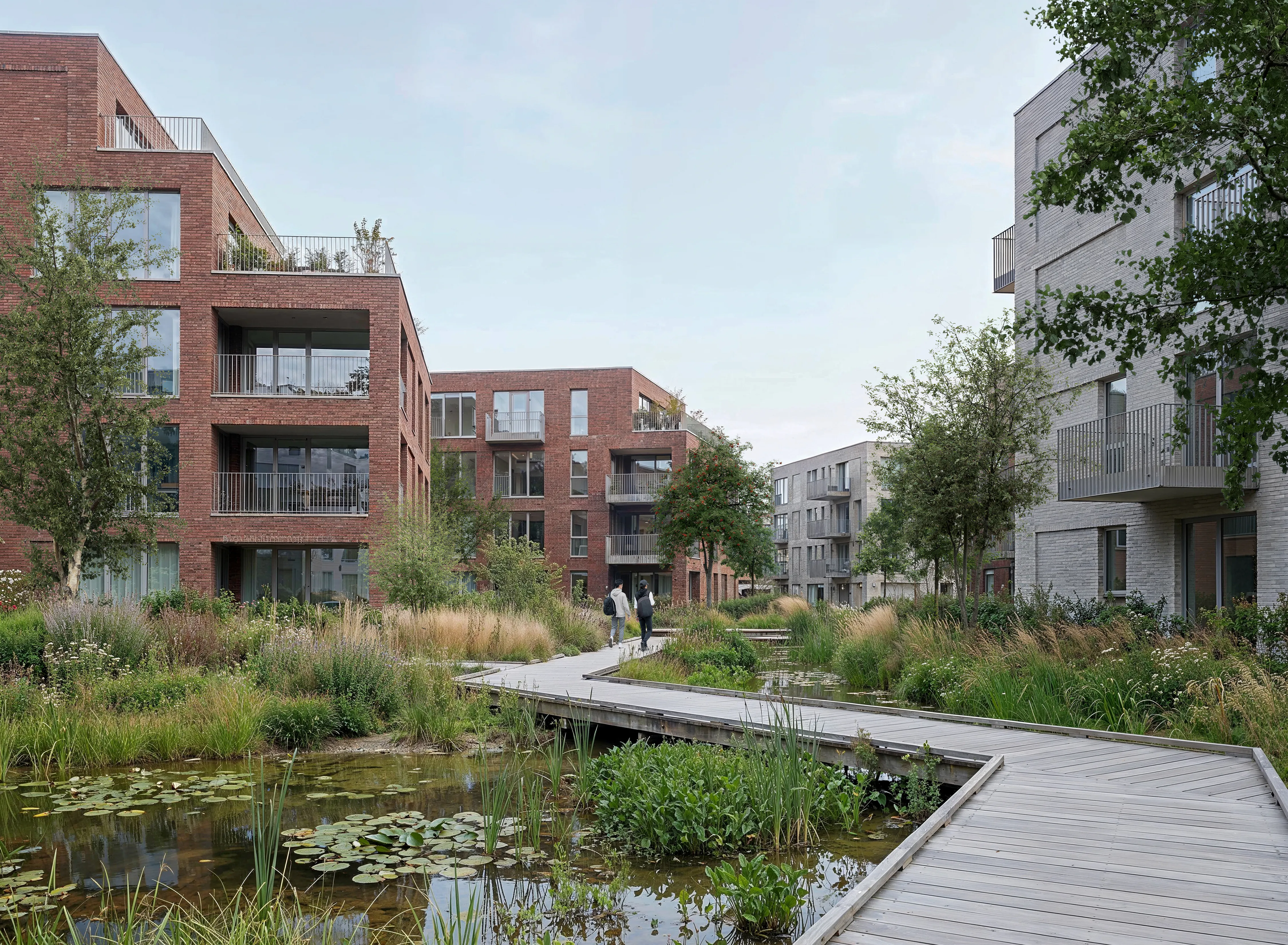 Brick courtyard housing at Odenseed, with balconies and a timber boardwalk crossing a planted rainwater pond.
